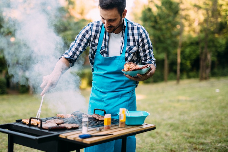 Handsome happy male preparing barbecue outdoors for friends