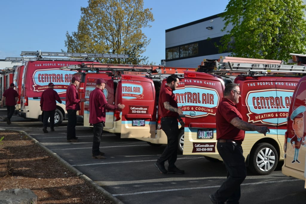 Photo of several Central Air HVAC technicians opening the backs of a fleet of branded vans