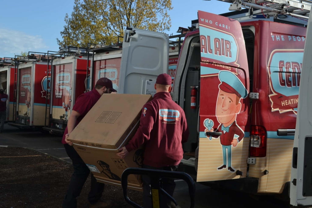 Two Central Air furnace technicians loading a furnace into a Central Air vehicle. 