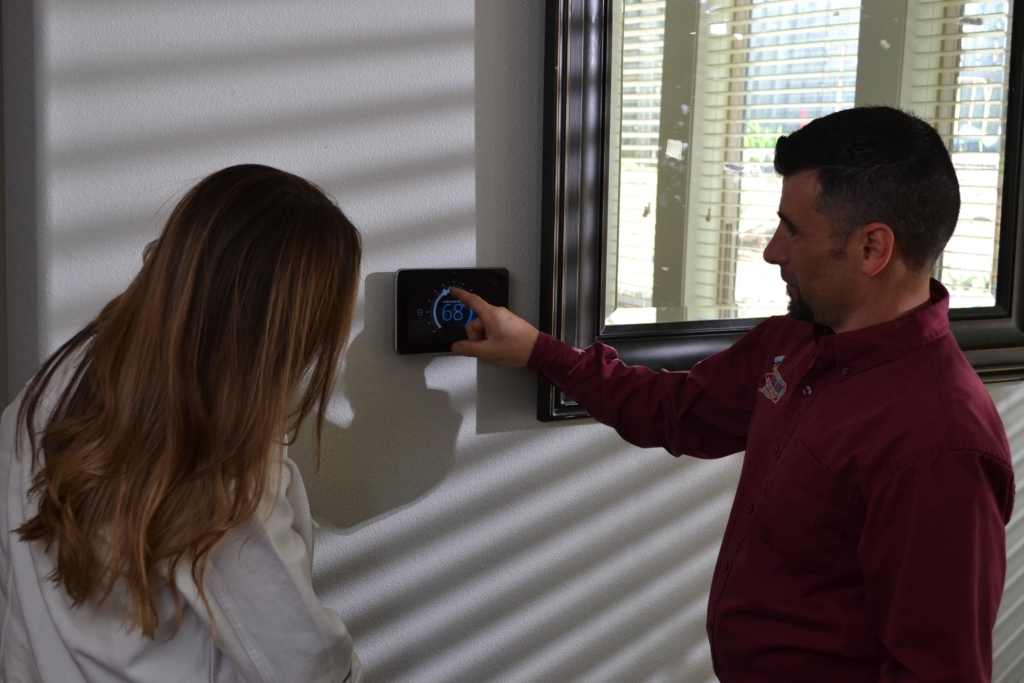 Central Air HVAC technician showing heat pump settings on thermostat to a customer.