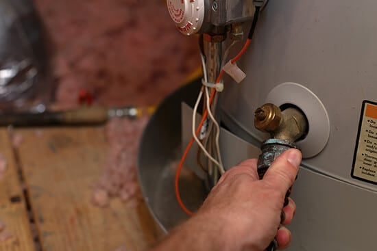 HVAC technician professionally flushing a water heater with a hose in Portland Oregon