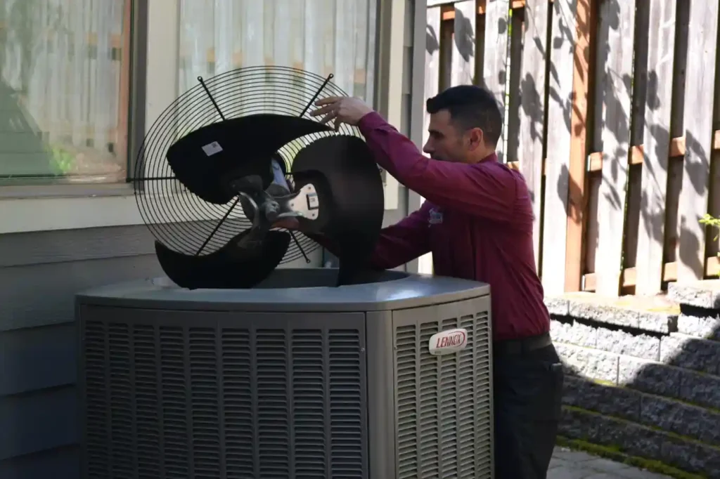 Technician inspecting and cleaning an outdoor condenser fan during a wildfire smoke in Portland.