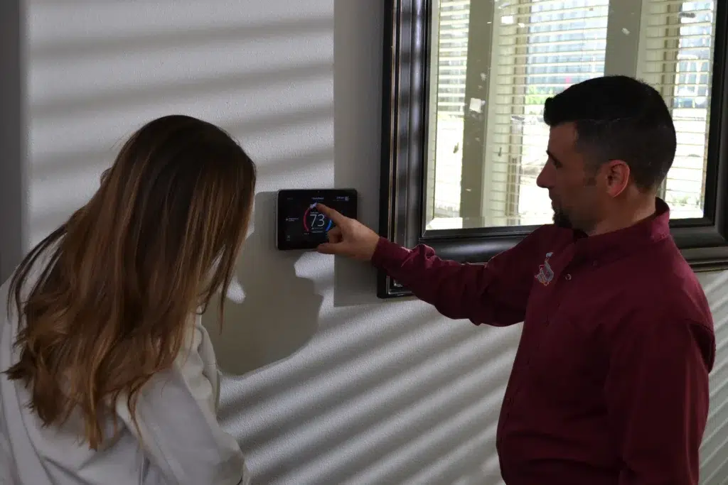 Technician demonstrating smart thermostat controls to help a homeowner understand heat pump backup heating settings.